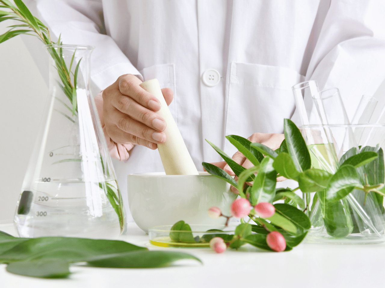 Person in a lab coat with a mortar and pestle, surrounded by greenery and scientific equipment.
